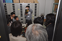 建物内の通路で参加者たちが設備を見学しながら説明を受けている写真