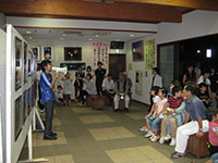 展示室で参加者たちが壁の展示を見ながら解説を聞いている写真