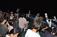 夜の屋外で参加者たちが望遠鏡を使って星空を観察している写真