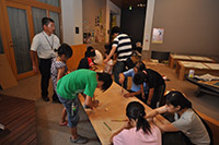 室内で子供たちが床に集まって体験活動に取り組んでいる写真