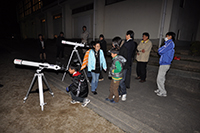 夜の屋外で親子や参加者たちが順番に望遠鏡をのぞいて星空を観察している写真