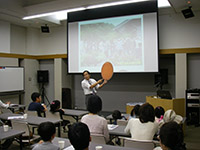 会議室の前方で講師が資料を示しながら参加者たちに向けて解説を行っている写真