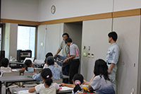 会議室の前方で講師と職員が子供たちに向けて説明を行っている写真