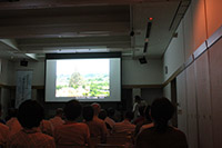 暗い室内で参加者たちがスクリーンに映された風景写真を見ている写真