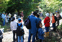 森林の中で親子や参加者たちが集まって観察や説明を受けている写真