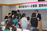 会場の前方で子供たちが並び講師から修了証や記念品を受け取っている写真