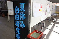 夏休み自由研究と書かれたパネルとホワイトボードに展示された自由研究の写真