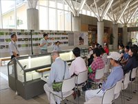 ガラスのショーケースの前の椅子に男女が並んですわり話を聞いている写真