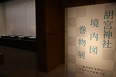 薄暗い部屋と入口に置かれた胡宮神社境内図巻物展と書かれた案内板の写真