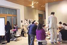 部屋の中で床に座る複数の参加者と立ち上がり説明をしている男性の後ろ姿の写真