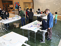 大きな白色の机の上でアート作品を制作する子供たちと保護者たちの写真