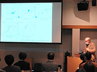 スクリーンの横で下を向いてマイクを持ち説明をする男性の写真
