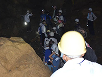 暗がりの中ヘルメットを着用した十数人の参加者が集まっている様子の写真