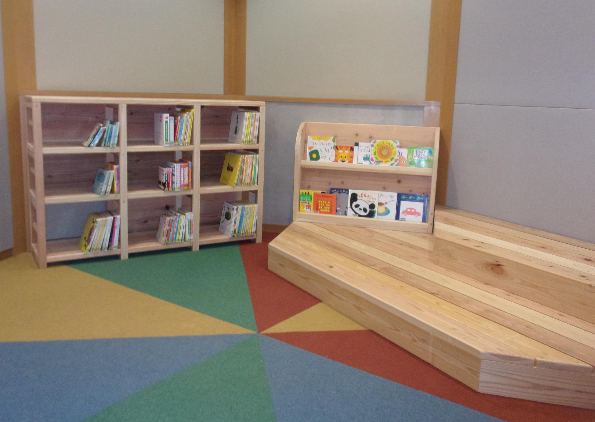 絵本用の低い書棚と木製ステージがあるおはなしのへやの写真