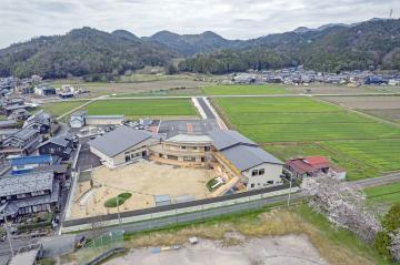 周りを田んぼに囲まれた園庭のある建物の写真