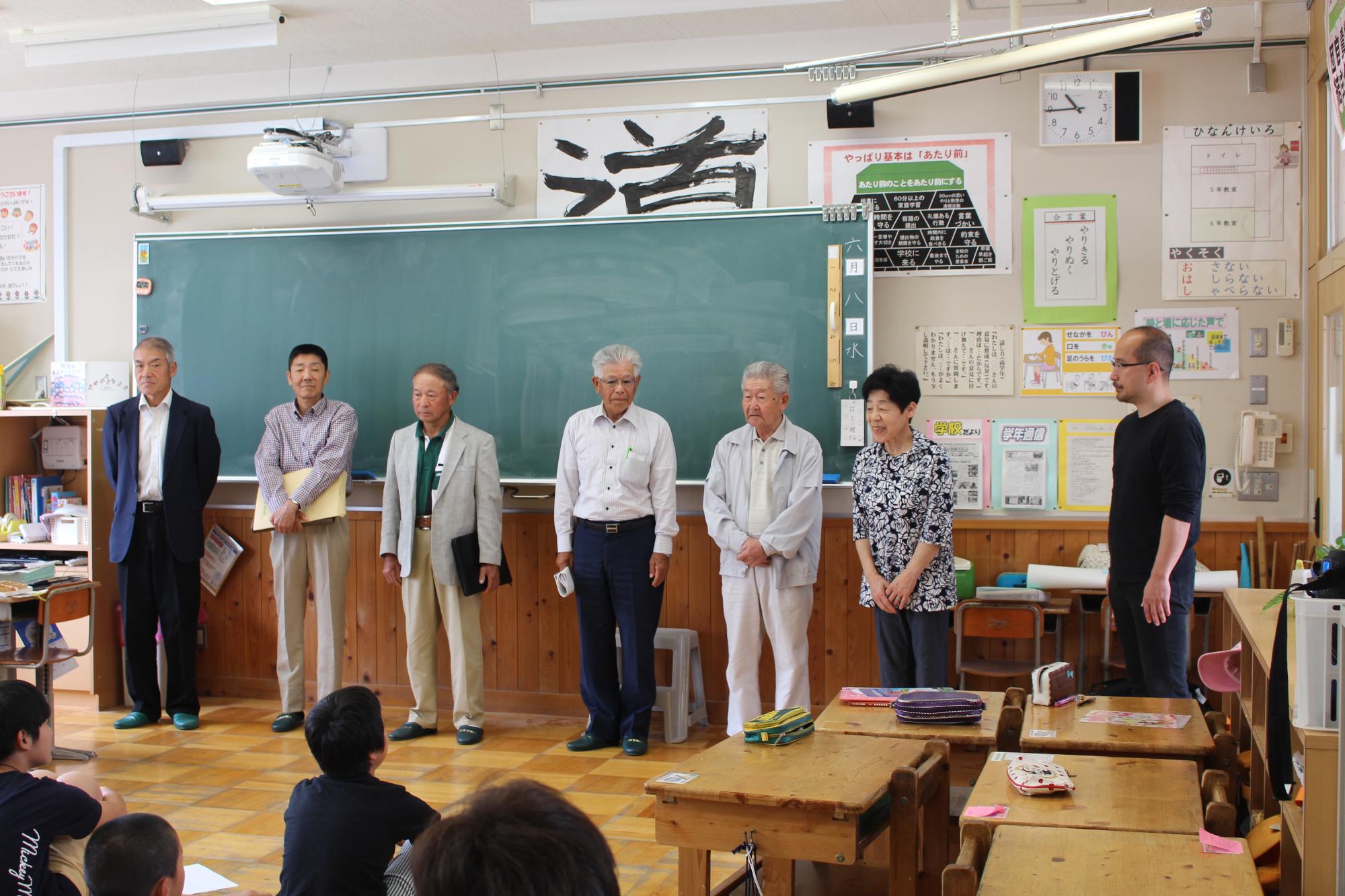 黒板の前に並んでいる6人の写真