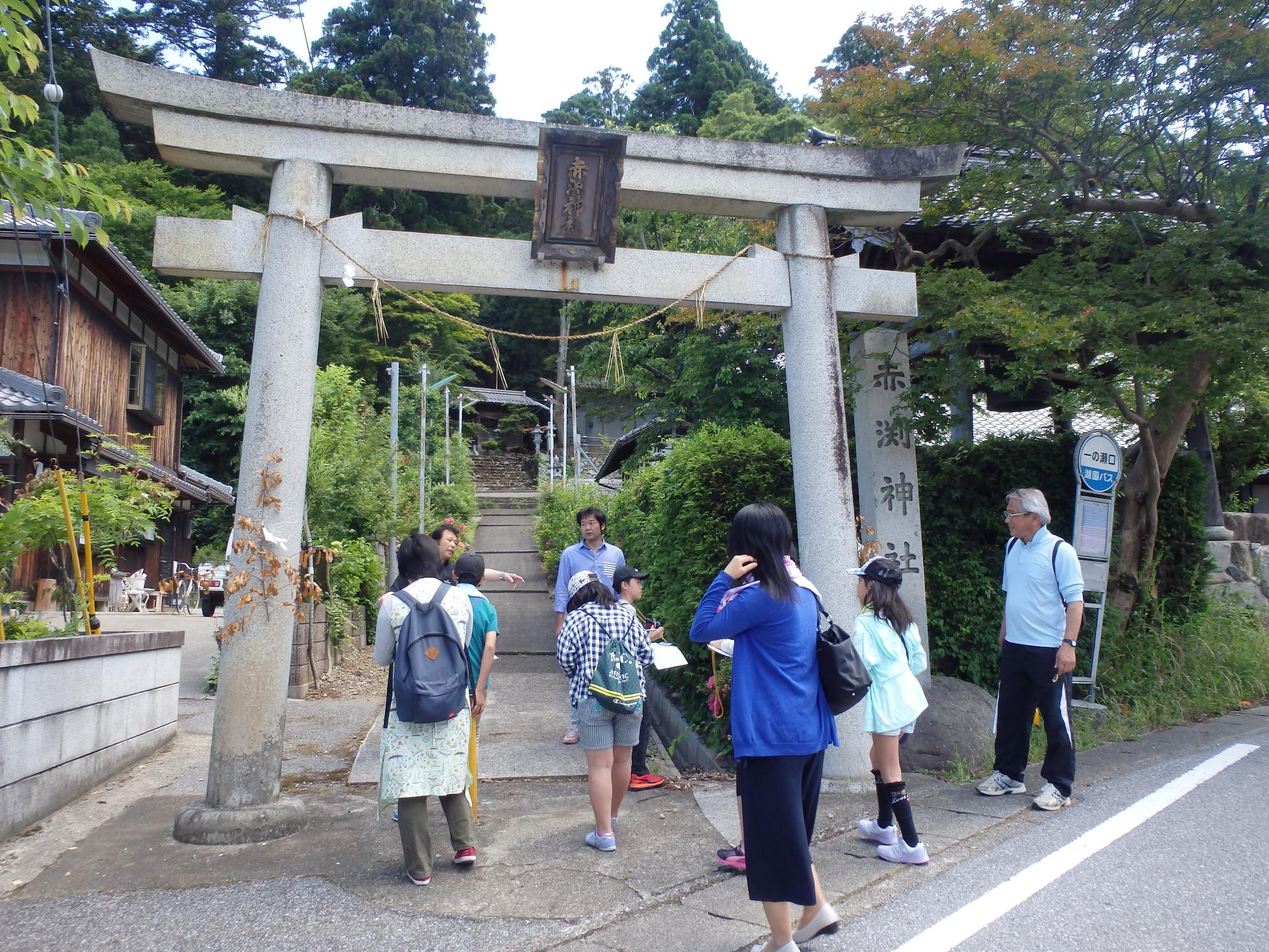 神社の鳥居の前に集まっている数名の大人と子供たちの写真