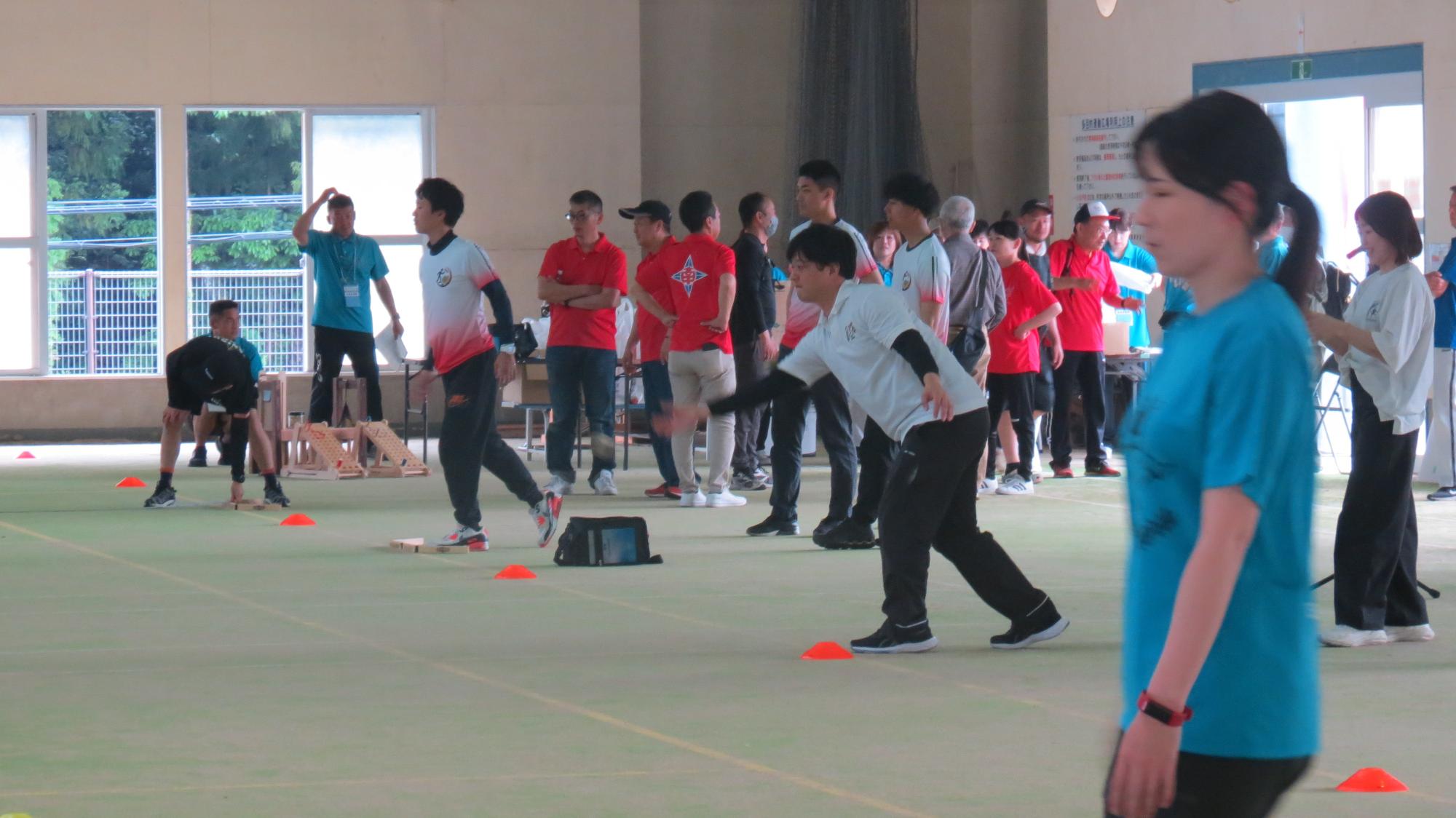 屋内会場で参加者たちがモルック競技に挑戦している様子を横から写した写真