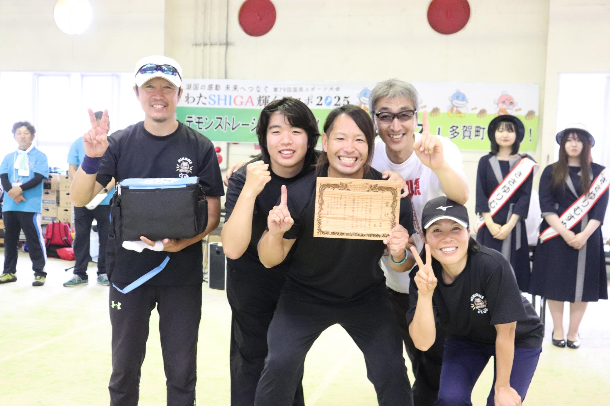 屋内会場で表彰状を手にした彦根モルッククラブのメンバーが集合して記念撮影している写真