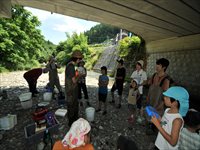 橋の下の河原で親子や参加者たちが集まって水辺の生き物を調べている写真