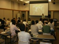 公民館の会議室で参加者たちがスクリーンを見ながら講義を受けている写真