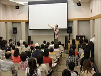 公民館の会議室で講師がステージ前に立ち参加者たちに向けて講演を行っている写真