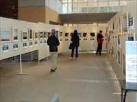 囲むように設置された複数のホワイトボードと飾られた展示物を鑑賞する複数の男女の写真