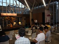 施設内のホールで参加者たちが椅子に座り演奏会や講演の開始を待っている写真