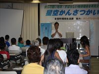 会場の前方で講師が参加者たちに向けて身振りを交えながら講演を行っている写真