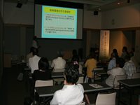 会議室で参加者たちがスクリーンに映された資料を見ながら講義を受けている写真