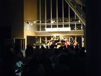 夜のホールで参加者たちがステージ上の演奏を鑑賞している写真