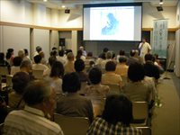 会議室で参加者たちが映像資料を見ながら解説を聞いている写真