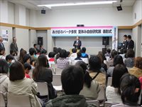 会場の前方で関係者が並び参加者たちに向けて開会の挨拶をしている写真