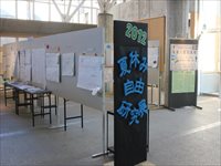 夏休み自由研究展と書かれたパネルと様々な自由研究の作品が飾られているホワイトボードが並んでいる様子の写真