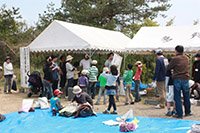 テントとブルーシートが設置された屋外に集まる人々の写真