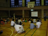 薄暗い体育館で座って前方のスクリーンを見ている子供たちの写真