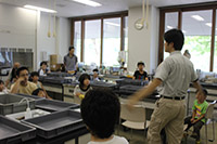 座っている子供たちと前で話す男性を前方から写した写真