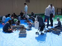 体育館の床にシートを敷いた会場で親子や児童たちが道具を使って作業をしている写真