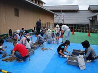 屋外の広場にシートを敷いた会場で親子や児童たちがグループに分かれて作業をしている写真