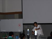 室内会場で講師が机の上の実験器具を使って説明をしている写真