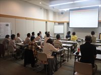 会議室で机に着席した参加者たちが前方のスクリーンを見ながら講義を受けている写真