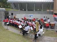 屋外ステージ前で演奏者たちが椅子に座って演奏の準備をしている写真