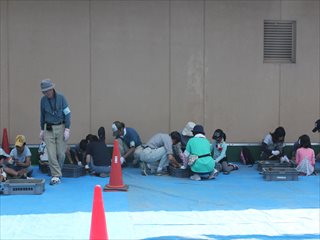 屋外の作業スペースで職員と親子がブルーシートの上に集まり発掘体験をしている写真