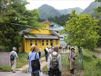 里山の古民家前で参加者たちが建物を囲みながら自然観察の説明を聞いている写真