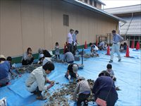 屋外の作業スペースで親子や参加者たちがブルーシートの上で体験活動に取り組んでいる写真