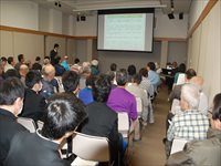 会議室で参加者たちがスクリーンに映された資料を見ながら研究発表を聞いている写真