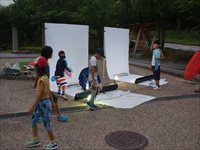 屋外で子供たちが白いパネルを使ってライトトラップの準備をしている様子の写真