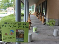 チェーンソー・アートと書かれたパネルと茶色い置物が2列に並んでいる写真