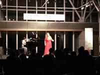 屋内ステージで歌手がマイクを持って歌い観客が鑑賞している写真