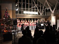 屋内ホールのステージで合唱団が並んで歌い観客が鑑賞しているコンサートの写真